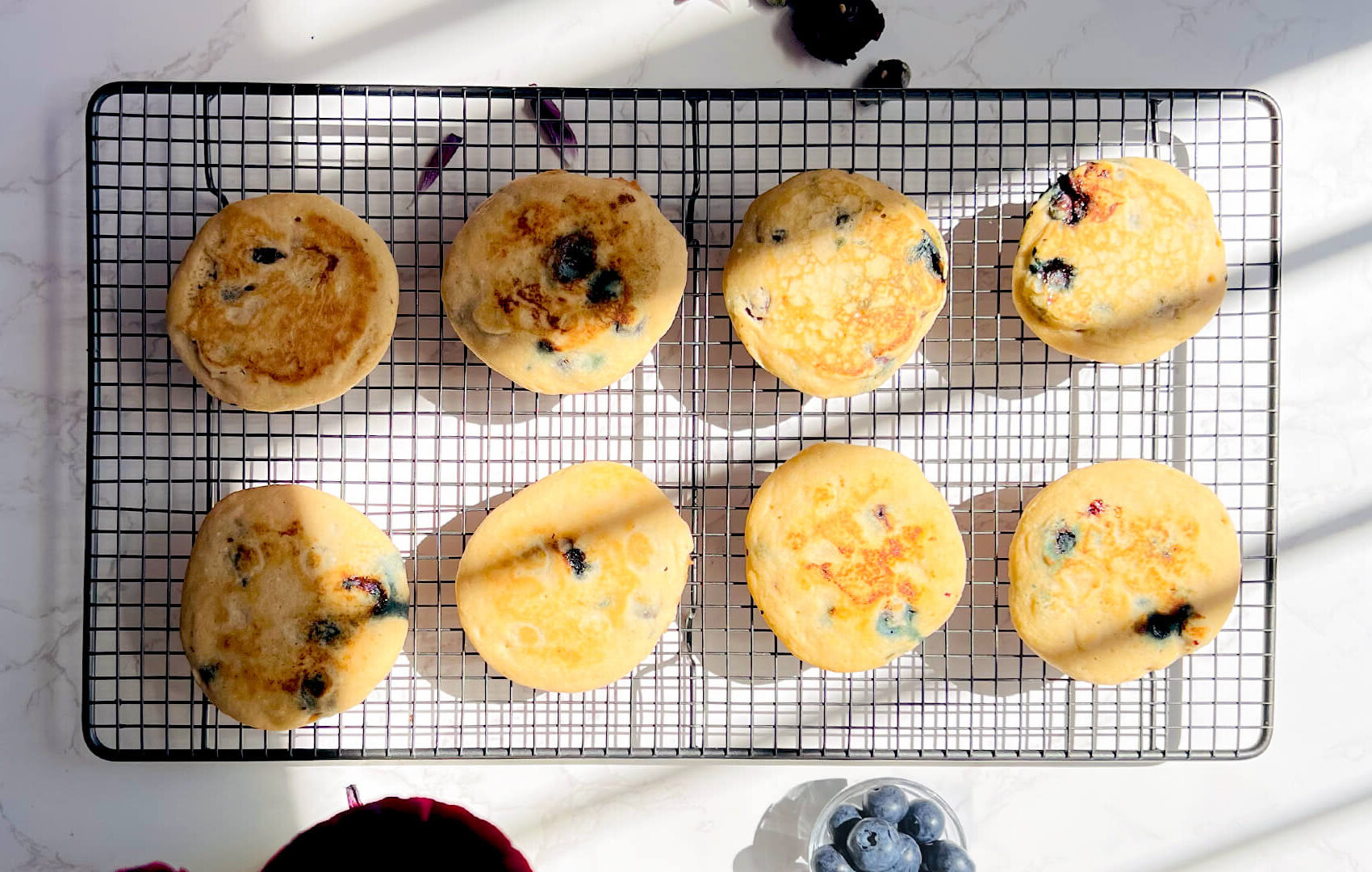 Freshly cooked paleo blueberry pancakes cooling on a wire rack, showing their thick fluffy texture, golden tops, juicy blueberries, and an easy healthy breakfast idea for meal prep or weekend brunch.