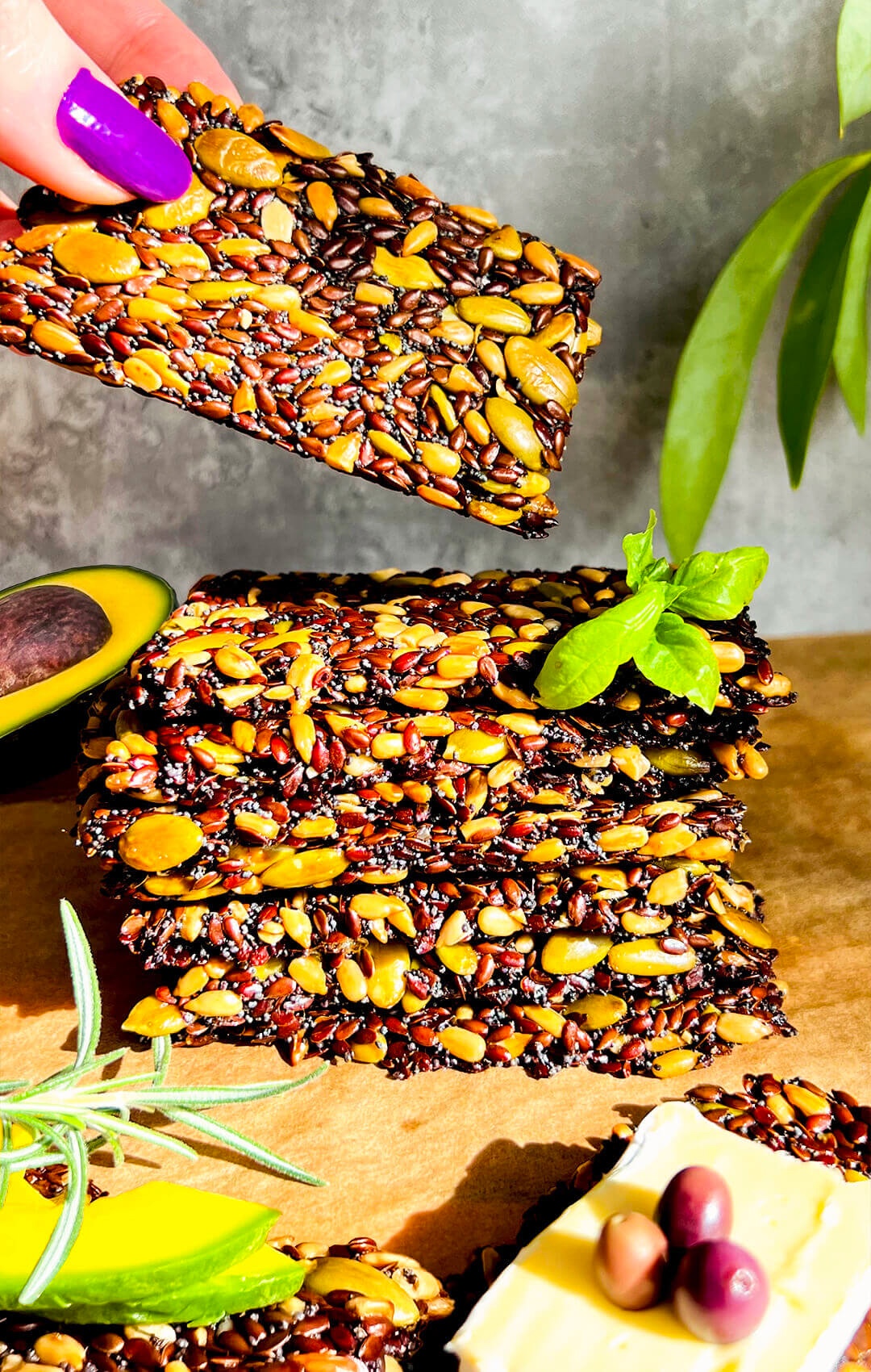 Easy seed crackers stacked with avocado, basil, rosemary and cheese, thin crispy healthy homemade gluten-free, keto, low-carb, vegan crackers made with wholesome seeds for snacking
