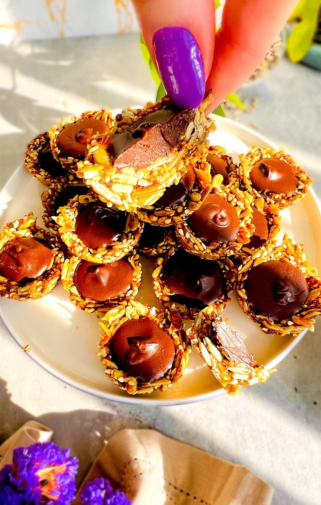 No-Oven Chocolate Tahini Seed Cup cut in half and held by hand, showing a crunchy golden toasted seed cup filled with a creamy, silky dark chocolate tahini centre. These healthy seed cups are pan-made, paleo, gluten-free, nut-free, dairy-free, oil-free, refined sugar-free, delicious, wholesome, and perfect for a chocolate snack, lunch box treat, or easy meal prep.