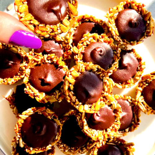 Crunchy Chocolate Tahini Seed Cups served on a plate, filled with silky, glossy dark chocolate tahini and made with toasted sunflower seeds, sesame seeds, shredded coconut, and honey. These no-oven healthy seed cups are paleo, gluten-free, nut-free, dairy-free, oil-free, refined sugar-free, rich, delicious, and perfect for chocolate cravings, lunch boxes, afternoon tea, or meal prep.