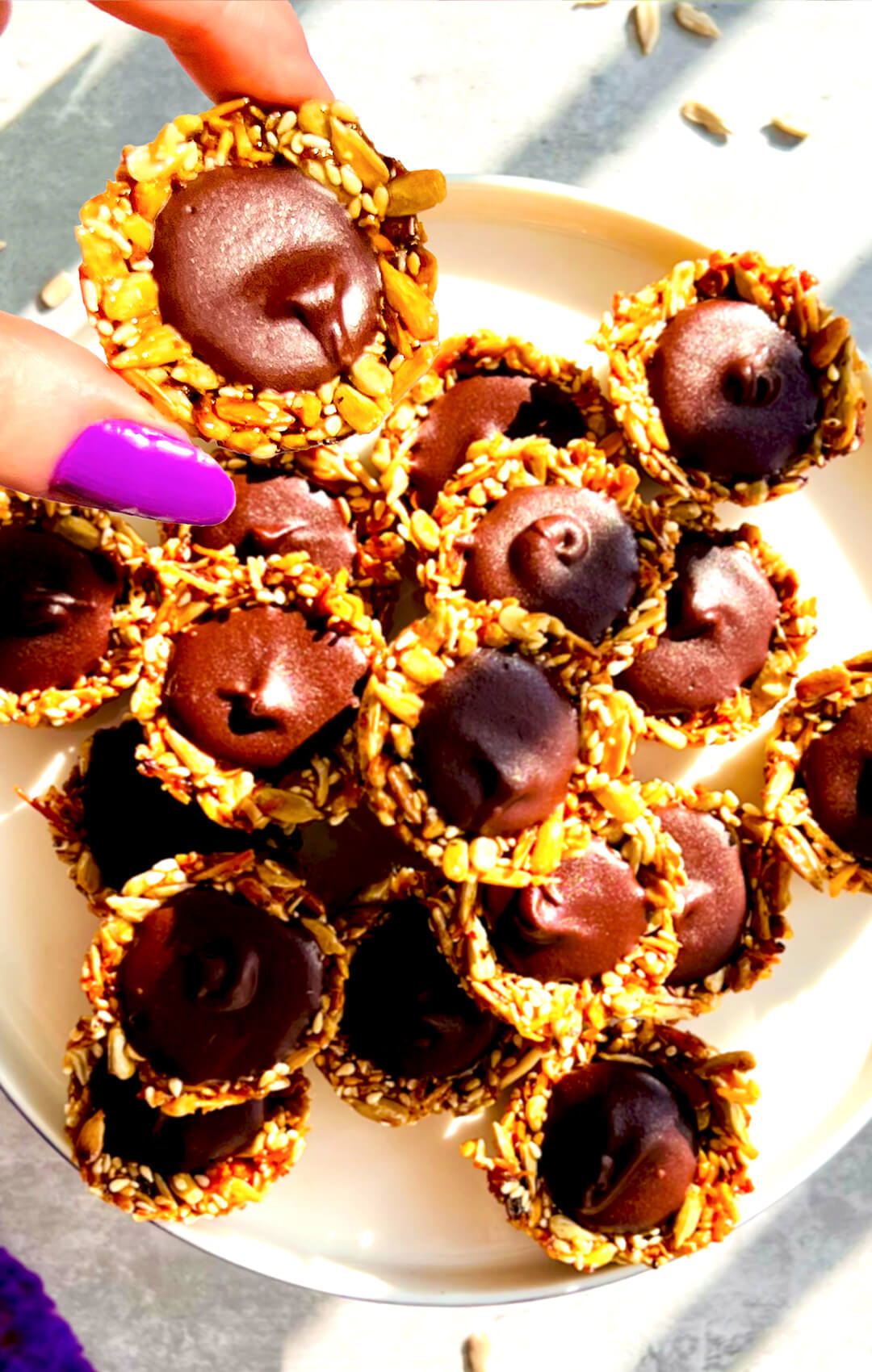 Crunchy Chocolate Tahini Seed Cups served on a plate, filled with silky, glossy dark chocolate tahini and made with toasted sunflower seeds, sesame seeds, shredded coconut, and honey. These no-oven healthy seed cups are paleo, gluten-free, nut-free, dairy-free, oil-free, refined sugar-free, rich, delicious, and perfect for chocolate cravings, lunch boxes, afternoon tea, or meal prep.