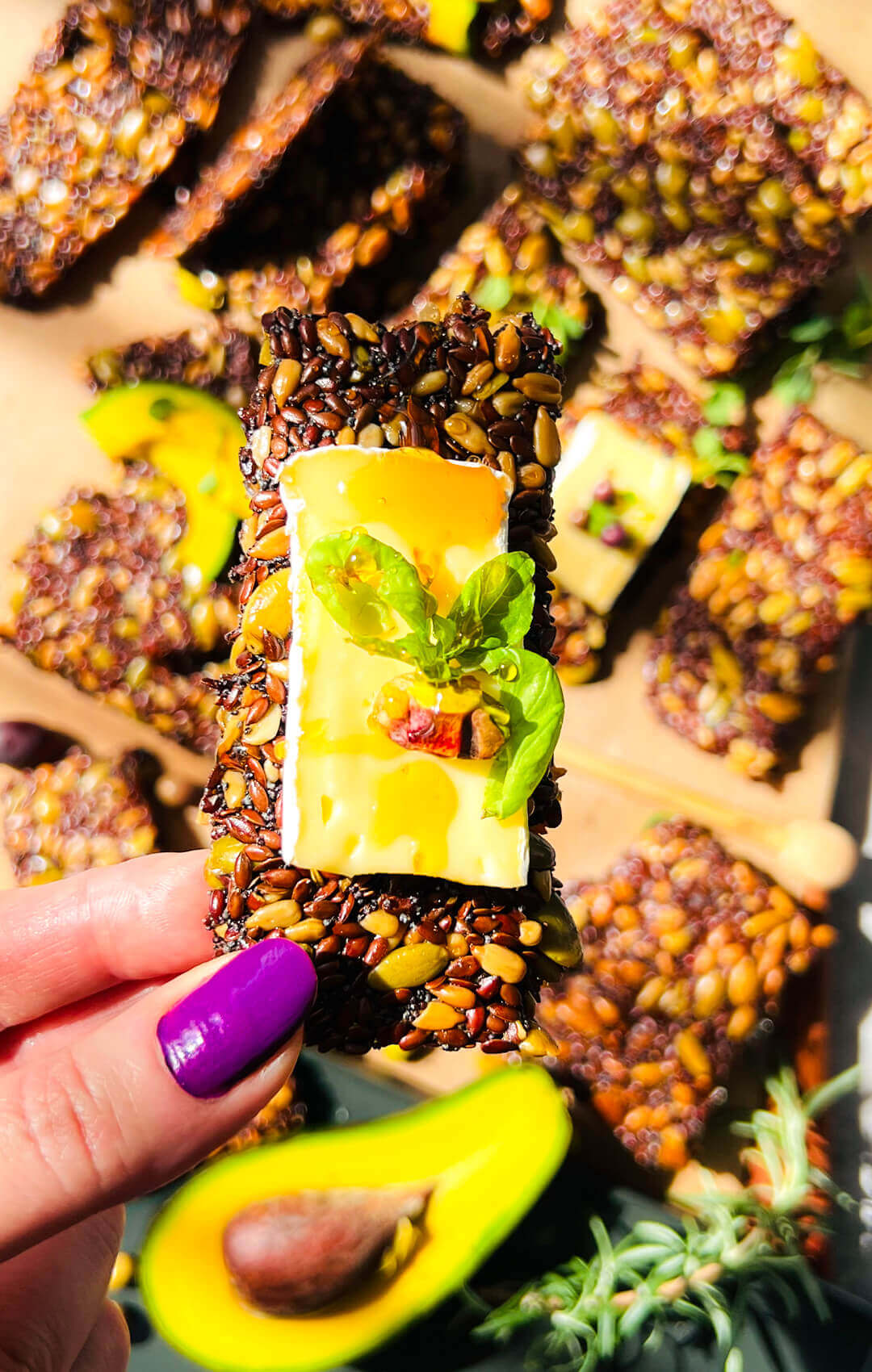 closeup to a thin crunchy seed cracker topped with creamy cheese, honey, fresh basil and pistachio, healthy homemade gluten-free, low-carb, vegan cracker for easy snacking. Quick and easy to make.