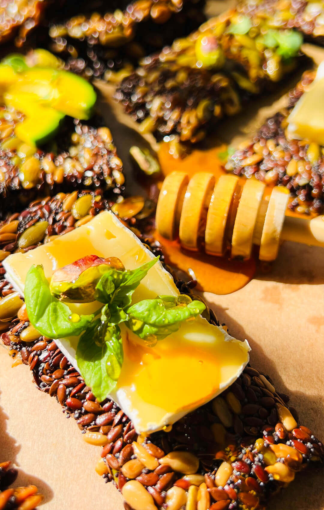 Close-up of a crispy seed cracker topped with cheese, honey, basil and pistachio, showing the thin crunchy texture of homemade gluten-free, low-carb, paleo seed crackers, quick and easy to make.