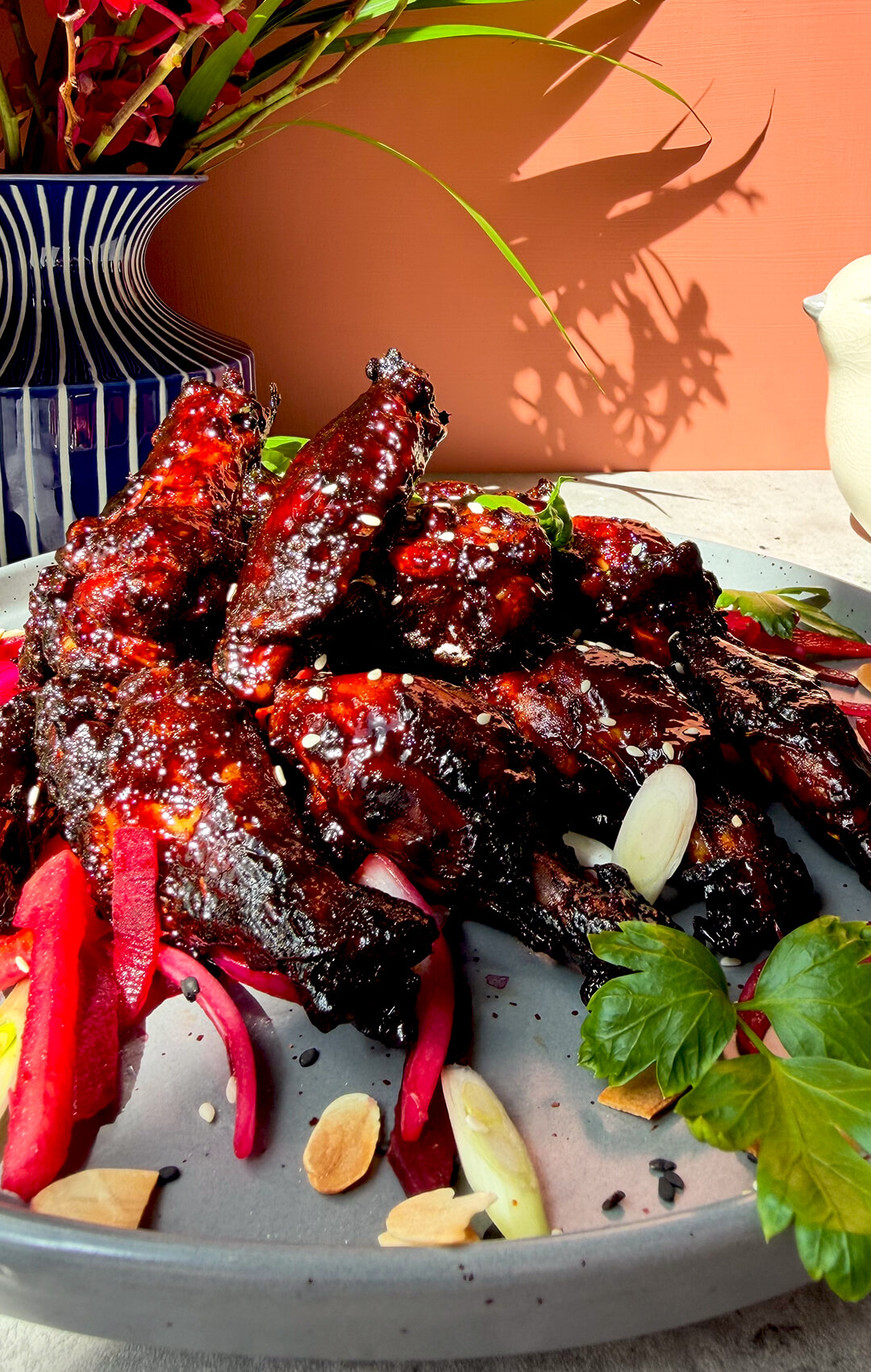 Crispy sticky honey soy wings coated in a dark red secret glaze and served with sesame seeds, fresh herbs, pink salad, spring onion, and toasted almonds. These air fryer chicken wings are healthy, dairy-free, high-protein, naturally sweetened with honey, glossy, smoky, sweet, savoury, caramelised, tender, juicy, and full of bold flavour.