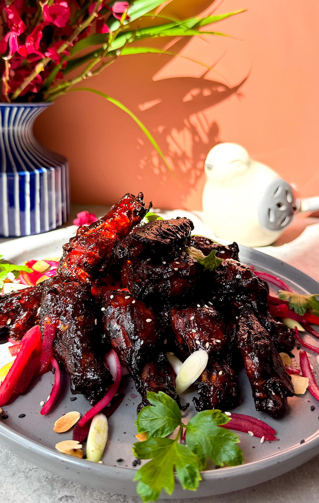 Sticky honey soy air fryer chicken wings served as a colourful dinner plate with glossy dark red glaze, sesame seeds, fresh herbs, pink salad, toasted almonds, and spring onion. These healthy crispy wings are naturally sweetened, dairy-free, high-protein, smoky, sweet, savoury, slightly spicy, juicy inside, caramelised outside, and easy to make at home.