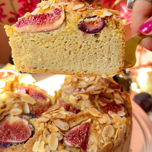 A thick slice lifted from a Fig Almond Olive Oil Cake, showing the tall soft crumb, fresh fig topping and golden sliced almonds. A healthy, guilt-free, gluten-free and keto-friendly cake made with almond flour, olive oil and wholesome ingredients for a moist dessert-like texture.
