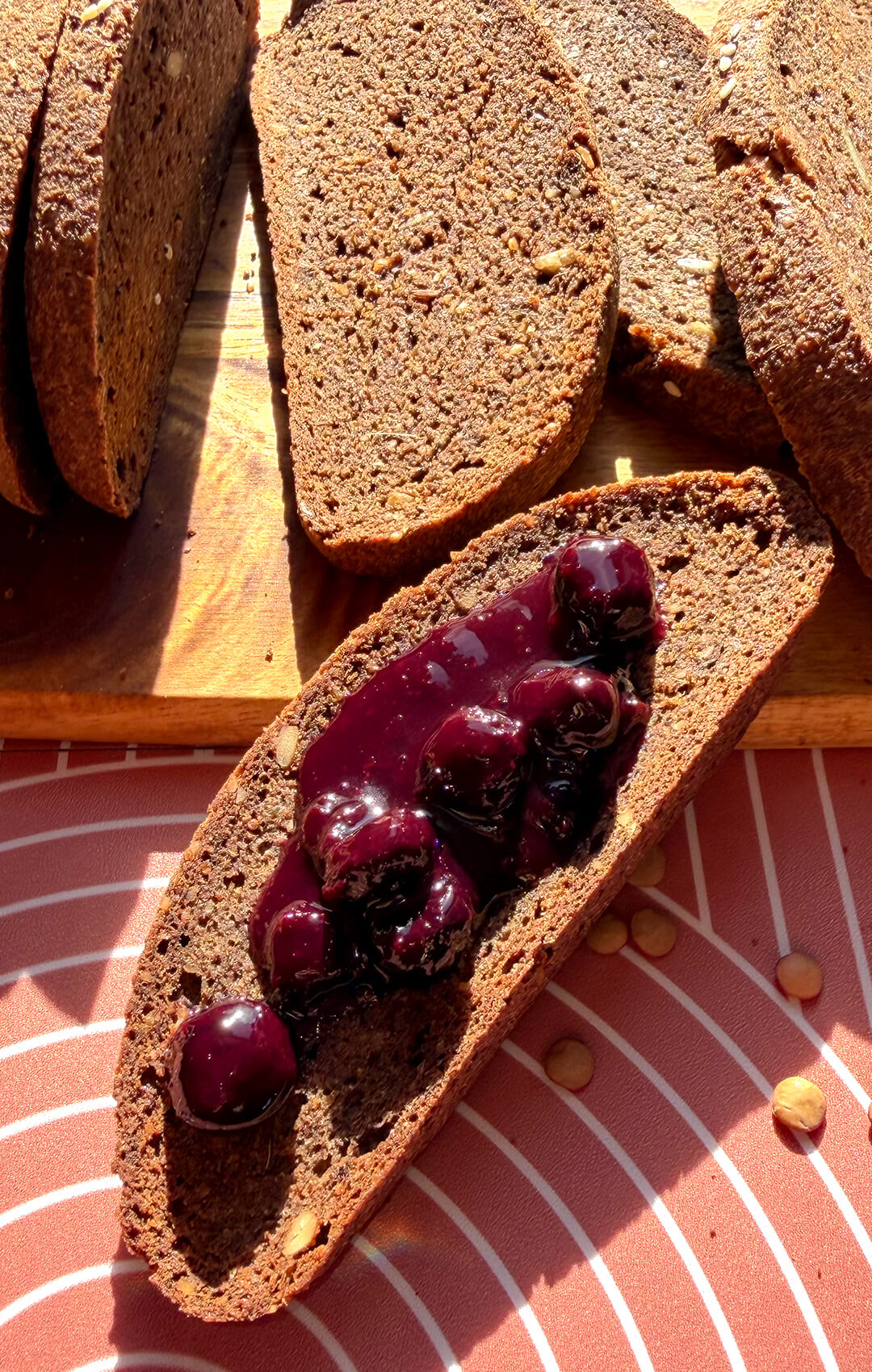 Rustic brown lentil bread served with glossy blueberry topping, showing a soft chewy crumb, small air pockets, and seeded texture. This gluten-free, flourless bread is yeast-free, egg-free, high in fibre, protein-rich, satisfying, easy to make at home, and tastes like real dark rye-style bread without tasting like lentils.
