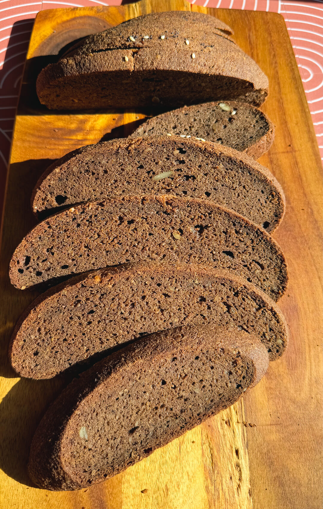 Sliced rustic brown lentil bread on a wooden board, showing a soft chewy crumb, small air pockets, golden crust, and hearty seeded texture. This gluten-free, flourless lentil bread is yeast-free, egg-free, high in fibre, protein-rich, easy to make at home, and has a delicious dark rye-style flavour and look without tasting like lentils, just like real rustic bread.