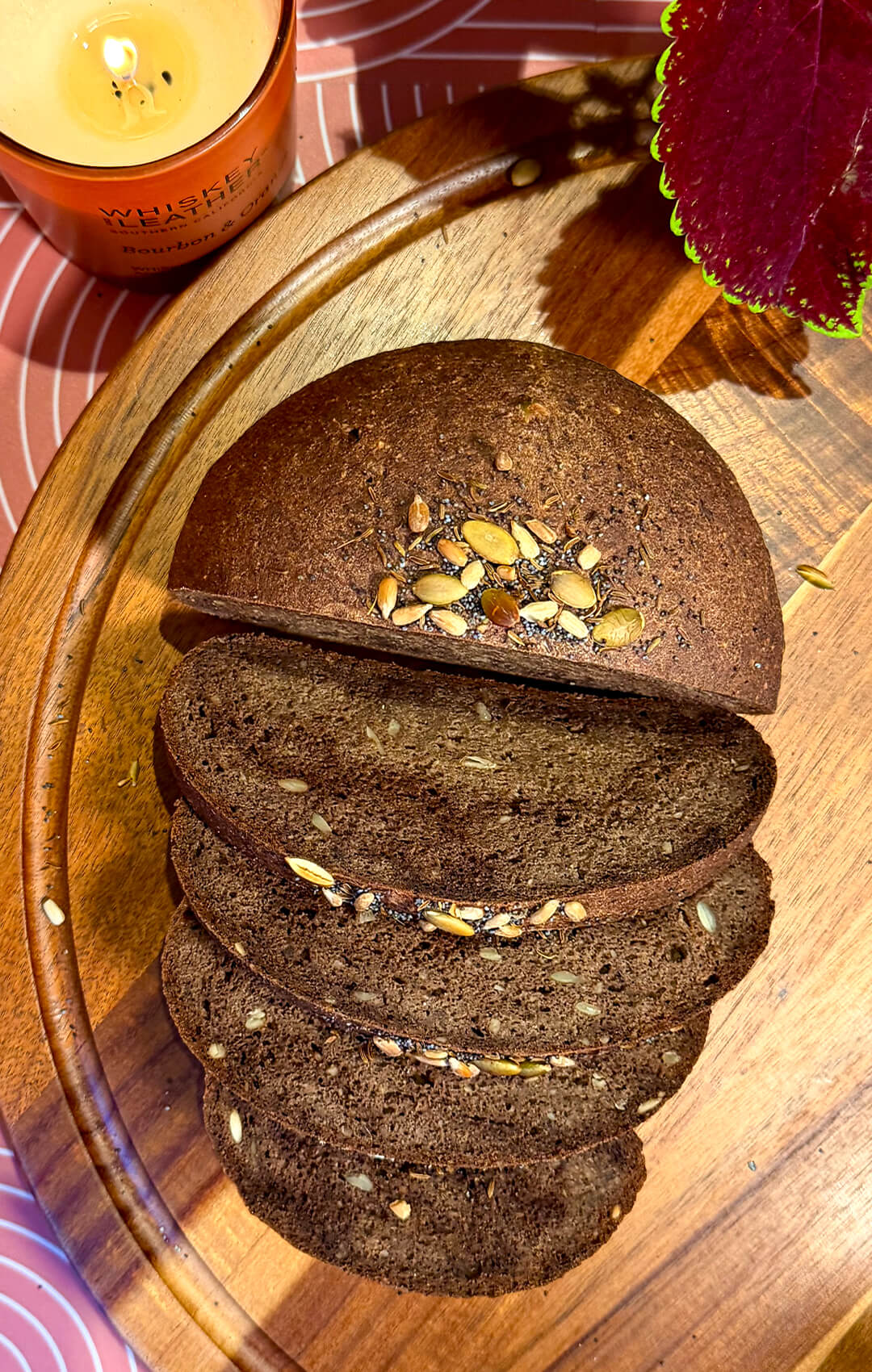 Sliced rustic brown lentil bread on a wooden board, showing a soft chewy crumb, small air pockets, seeded texture, and deeper dark rye-style colour from a little extra cocoa powder. This gluten-free, flourless bread is yeast-free, egg-free, high in fibre, protein-rich, satisfying, and tastes like real rustic bread without tasting like lentils.
