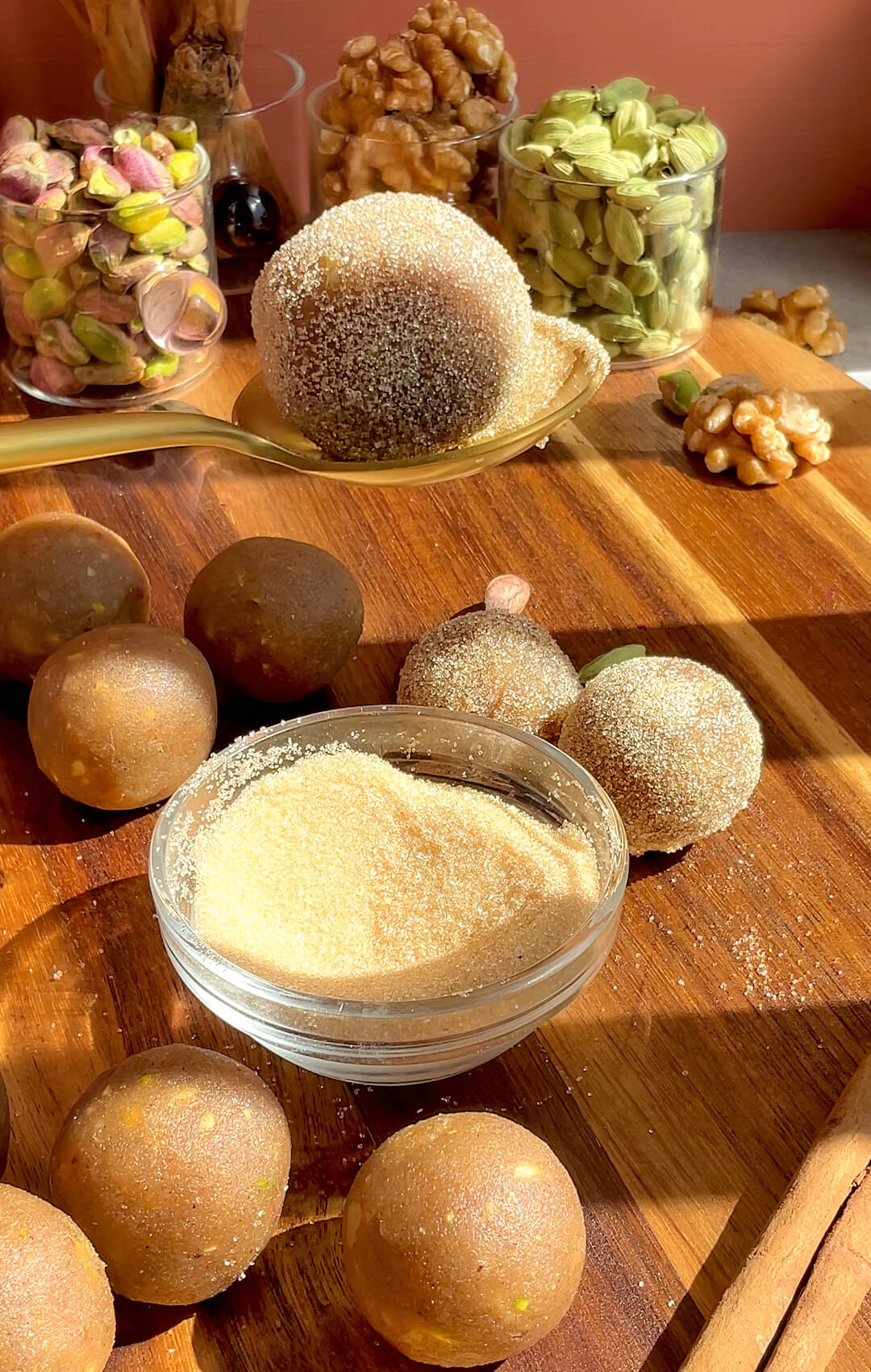 Healthy Baklava Bites being coated in golden monk fruit sweetener before filling and baking, with pistachios, walnuts, cardamom and cinnamon in the background. These gluten-free, grain-free, dairy-free and refined sugar-free baklava bites are naturally sweetened with honey, easy to make without filo pastry, crisp outside, soft and moist inside, and full of delicious nutty rose water flavour.