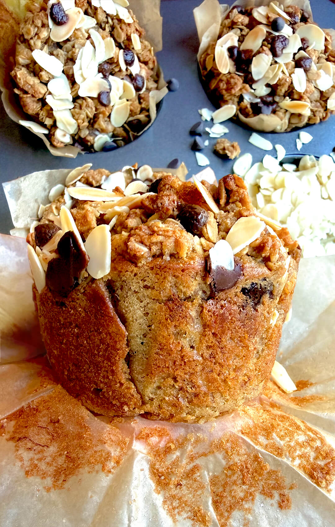 Close-up of a soft gluten-free banana bread crumble muffin with a golden bakery-style crumb, chunky oat almond topping, sliced almonds, and melted sugar-free chocolate chips. This delicious, dairy-free, refined sugar-free banana muffin is naturally sweetened, moist, satisfying, and perfect for a healthy breakfast or cozy homemade snack.