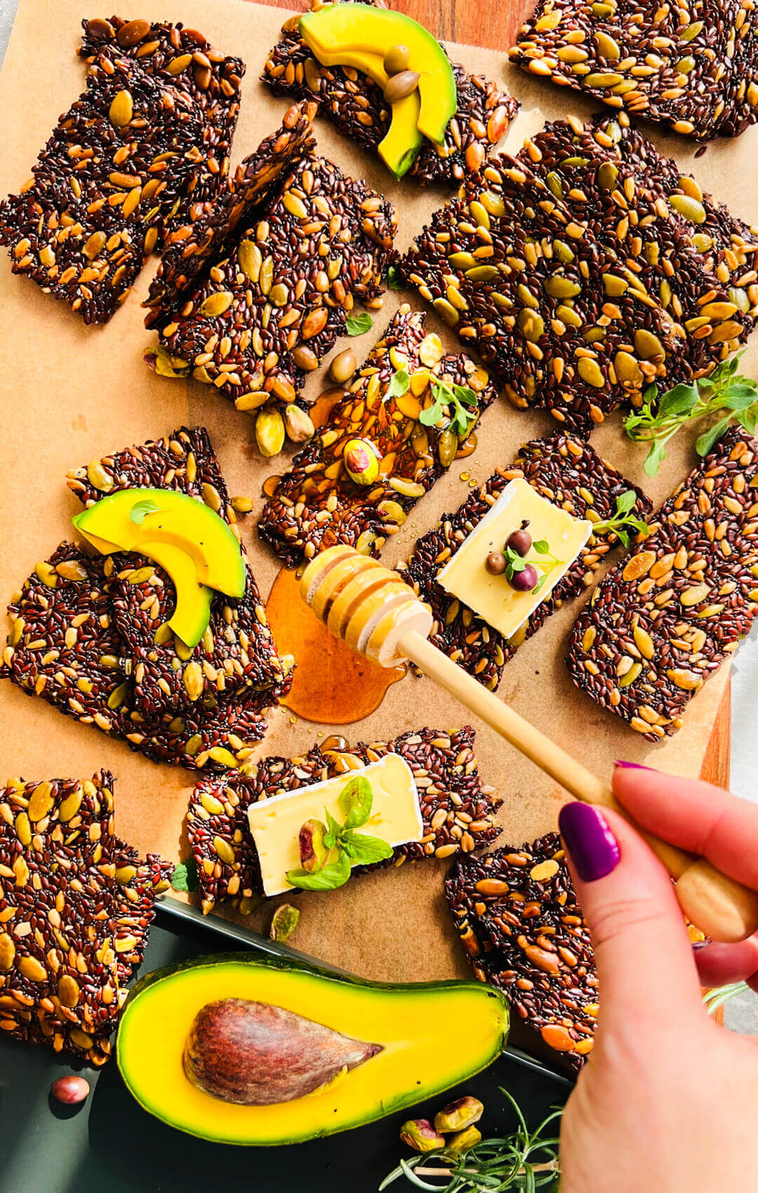 Easy thin and crispy seed crackers served on a snack board with avocado, cheese, honey, basil, rosemary and pistachios, crunchy healthy gluten-free keto crackers for dips and snacking