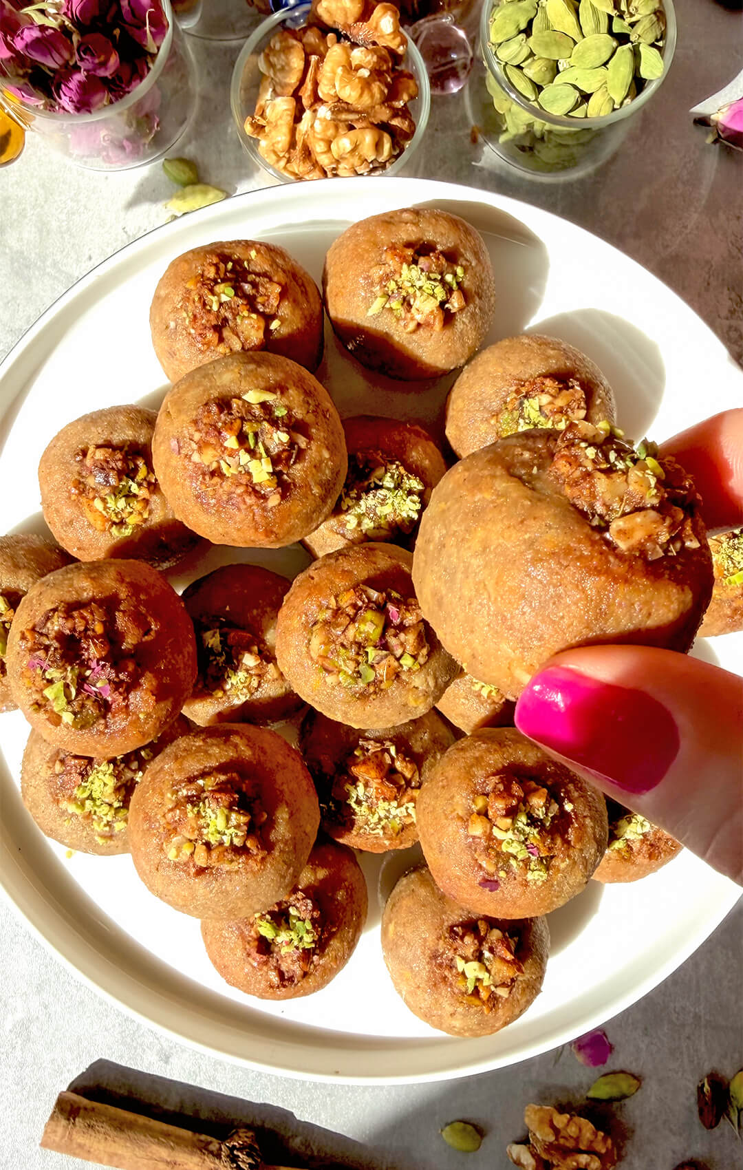 Close-up of Healthy Baklava Bites topped with pistachio walnut filling, with one bite held above the plate to show the golden, crunchy fragrant, nutty texture. These paleo, gluten-free, grain-free, dairy-free and refined sugar-free baklava bites are naturally sweetened with honey, made with almonds, walnuts, pistachios, rose water and warm spices, crisp outside, moist inside, and perfect for an easy healthy dessert or sweet snack.