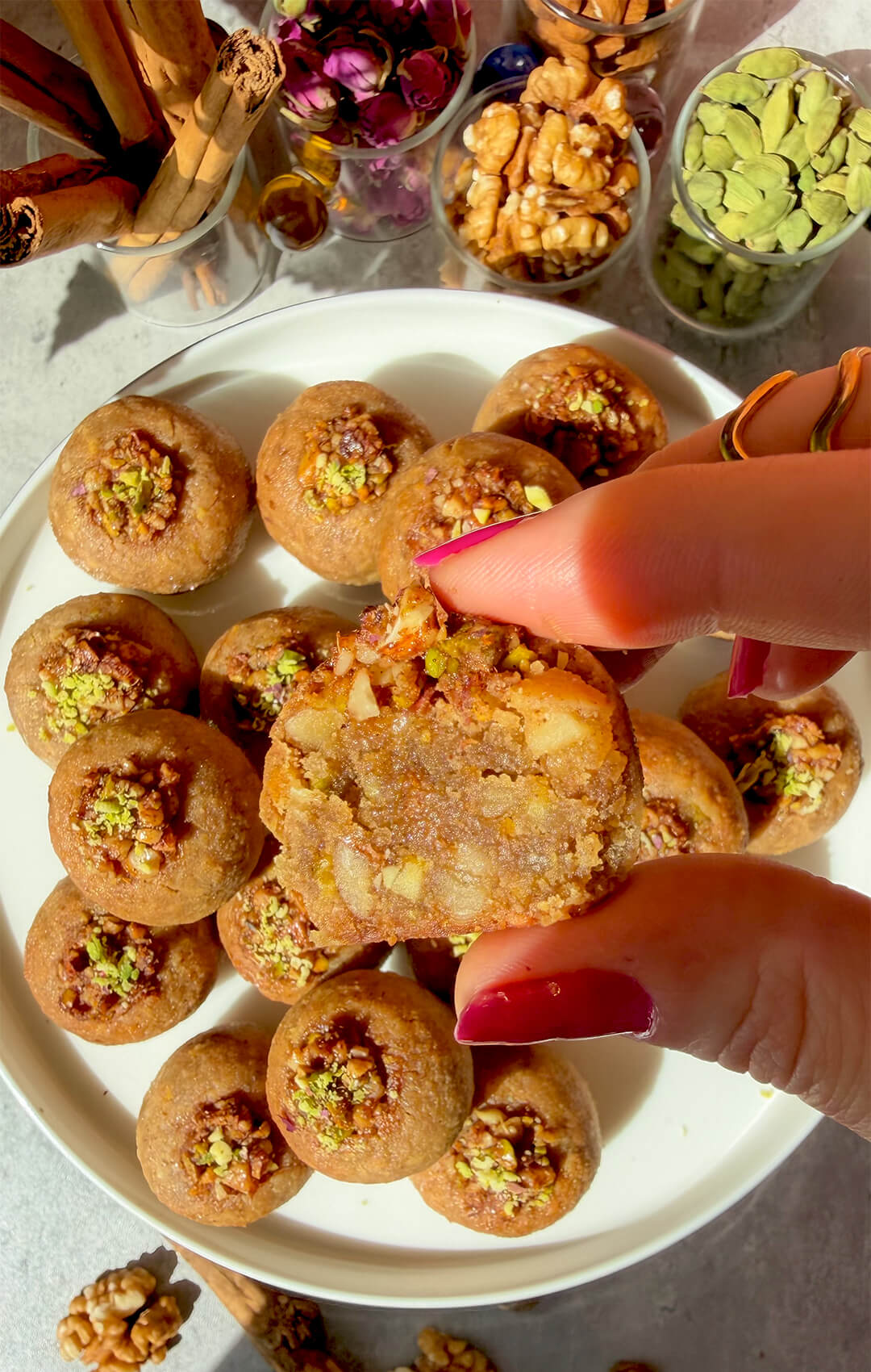 Healthy Baklava Bite held open to show the moist almond, walnut and pistachio centre, with golden baklava bites topped with pistachio walnut filling on a plate underneath. These gluten-free, grain-free, dairy-free and refined sugar-free, paleo baklava bites are naturally sweetened with honey, crisp outside, soft and moist inside, full of rose water, cardamom, cinnamon and warm spices, and perfect for a satisfying healthy sweet treat.