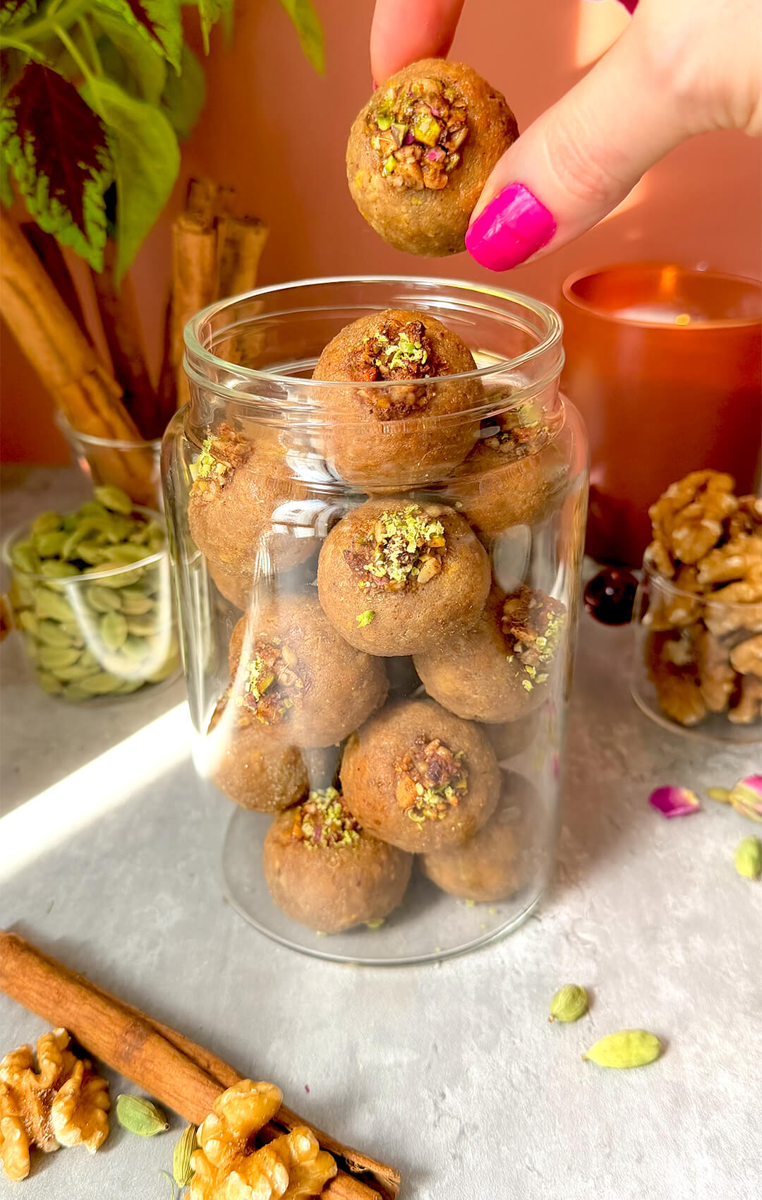 Healthy Baklava Bites stored in a glass jar with cinnamon sticks, cardamom pods, walnuts and rose petals around them. These easy make-ahead baklava bites are paleo, gluten-free, grain-free, dairy-free, oil-free, and refined sugar-free, naturally sweetened with honey, crisp outside, moist inside, and full of delicious almond, walnut, pistachio, rose water and warm spice flavour.