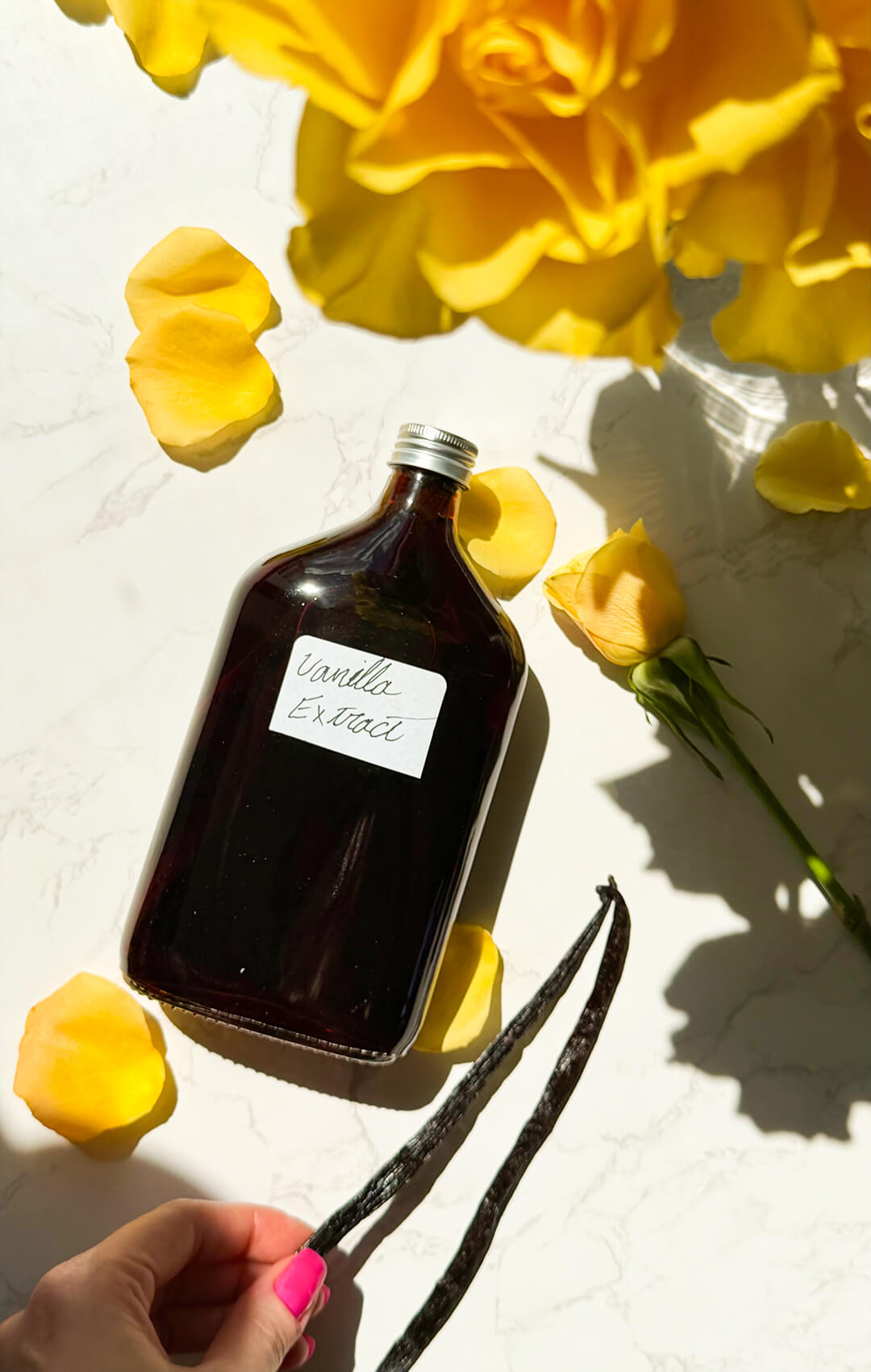 © Healthy Food by Annie. All rights reserved. No reuse, copying, editing, reposting, or redistribution without written permission. ark aged homemade vanilla extract in a glass bottle with Madagascar vanilla beans, yellow roses, and a gold spoon in natural sunlight. This easy 2-ingredient vanilla extract recipe takes less than 10 minutes to prepare and becomes a simple homemade baking staple with no added sugar or artificial flavours.