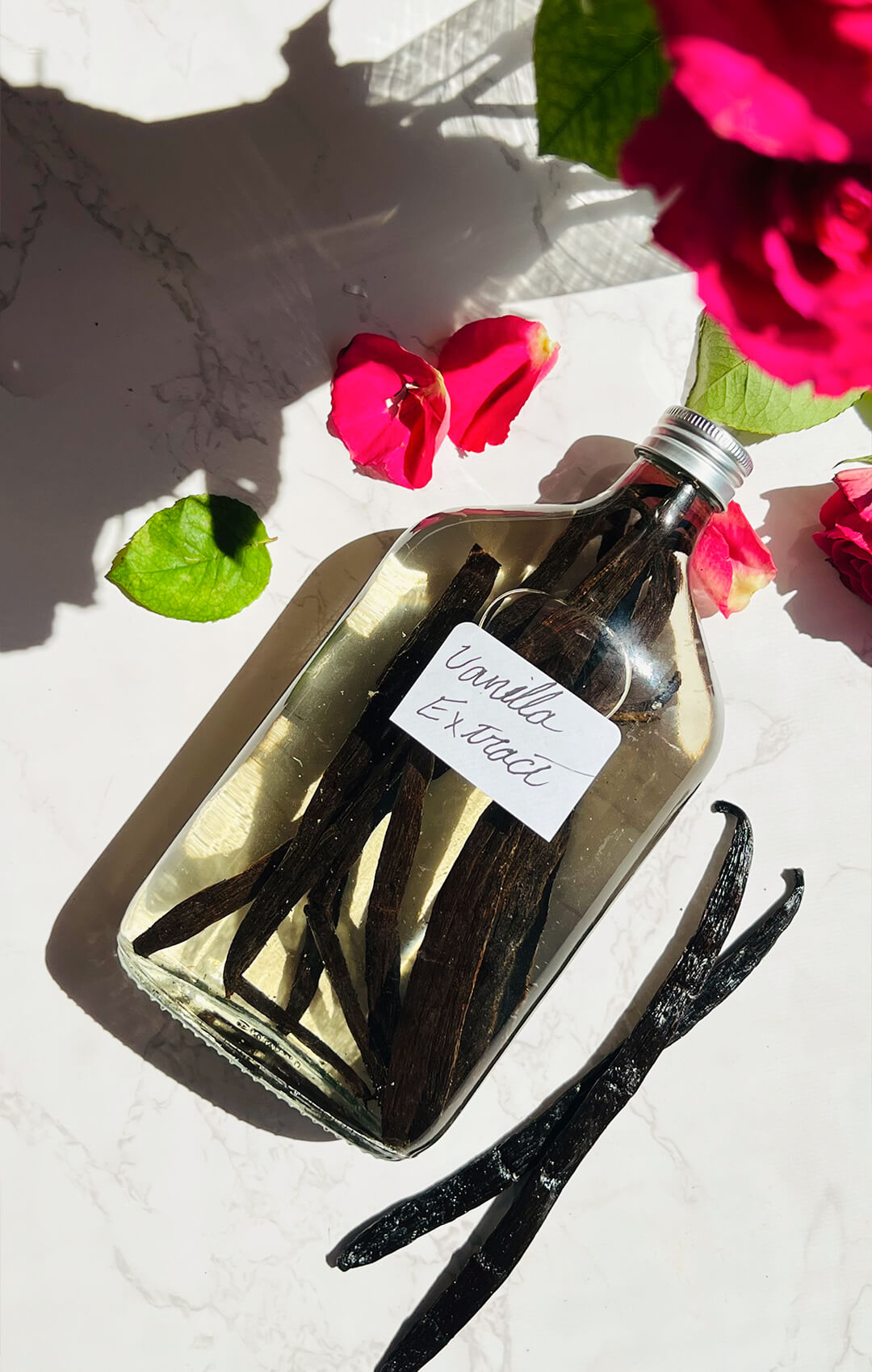 © Healthy Food by Annie. All rights reserved. No reuse, copying, editing, reposting, or redistribution without written permission. Homemade vanilla extract in a clear glass bottle with split Madagascar vanilla beans and rose petals, perfect for baking cakes, cookies, muffins, and desserts. Easy 2- ingredient with no added sugar, no artificial flavours, and rich real vanilla flavour.