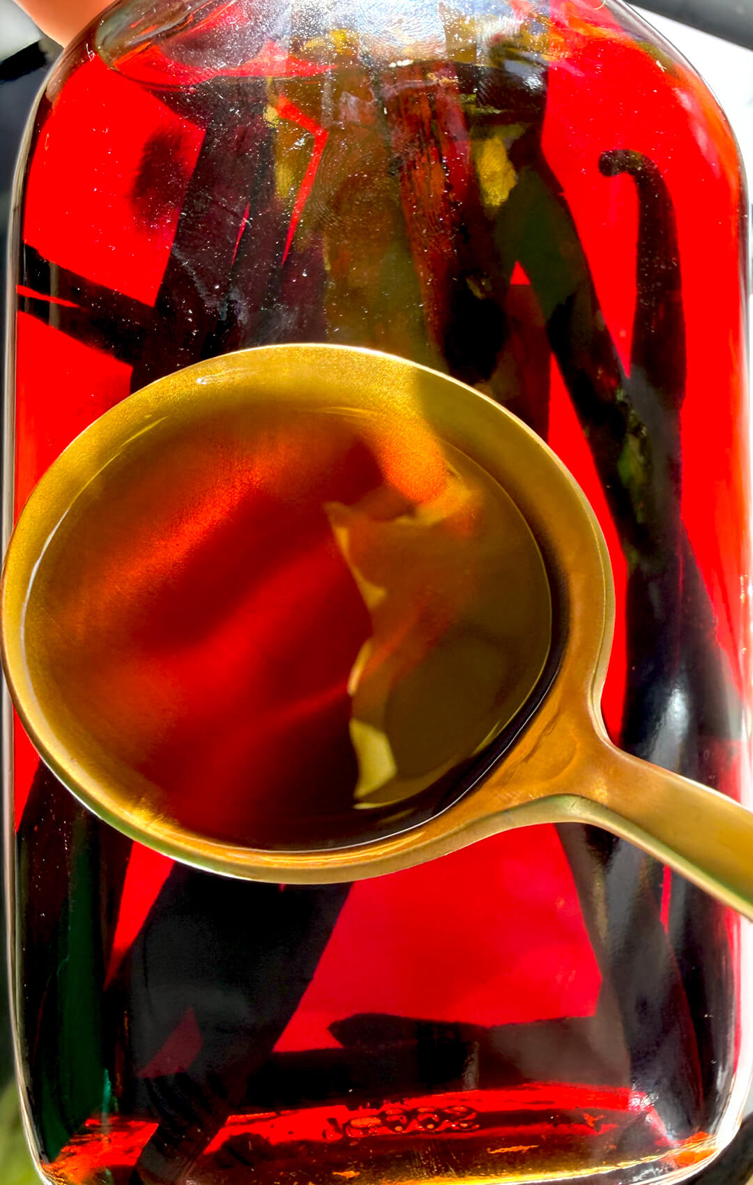 © Healthy Food by Annie. All rights reserved. No reuse, copying, editing, reposting, or redistribution without written permission. Close up of rich amber homemade vanilla extract in a spoon with vanilla beans inside the bottle, showing the deep colour of aged DIY vanilla extract. Made with only 2-ingridinat and so easy to make.