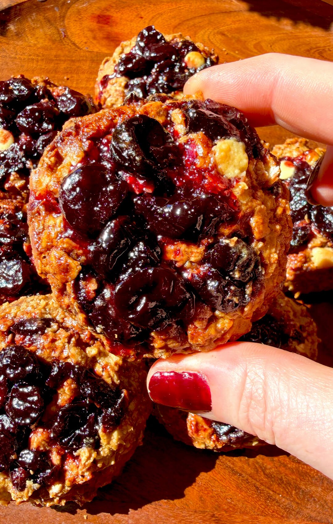Close up of a healthy peanut butter sour cherry oatmeal cookie with glossy homemade cherry filling, sugar-free white chocolate chips and golden caramelized edges, made with rolled oats and almond flour for a gluten-free, refined sugar-free cookie.