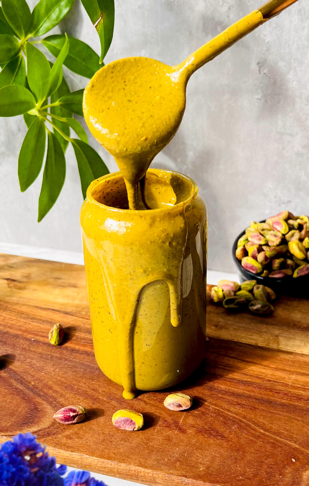 Glossy spoonful of homemade pistachio butter dripping back into a jar, showing the velvety smooth, drizzleable texture of this healthy one ingredient pistachio butter recipe.