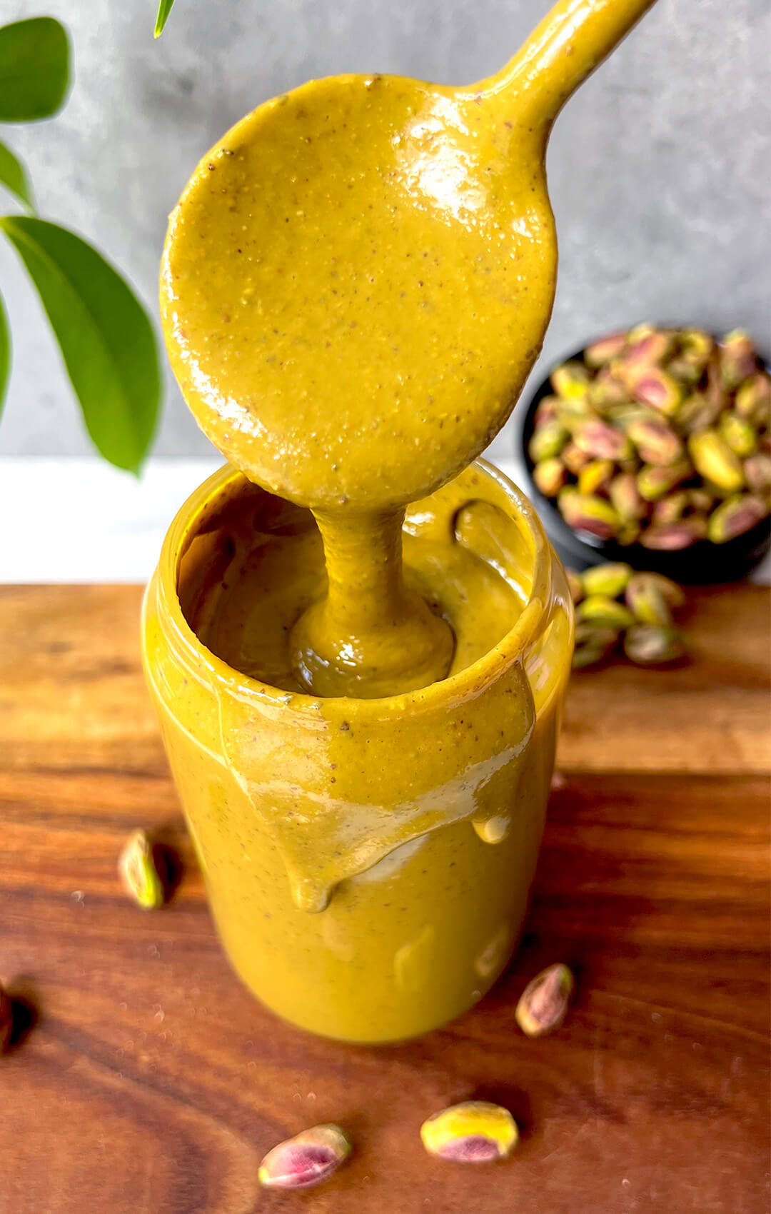 Close up of creamy homemade pistachio butter on a spoon above a jar, highlighting the rich pistachio flavour, silky texture, and naturally smooth healthy nut butter consistency.