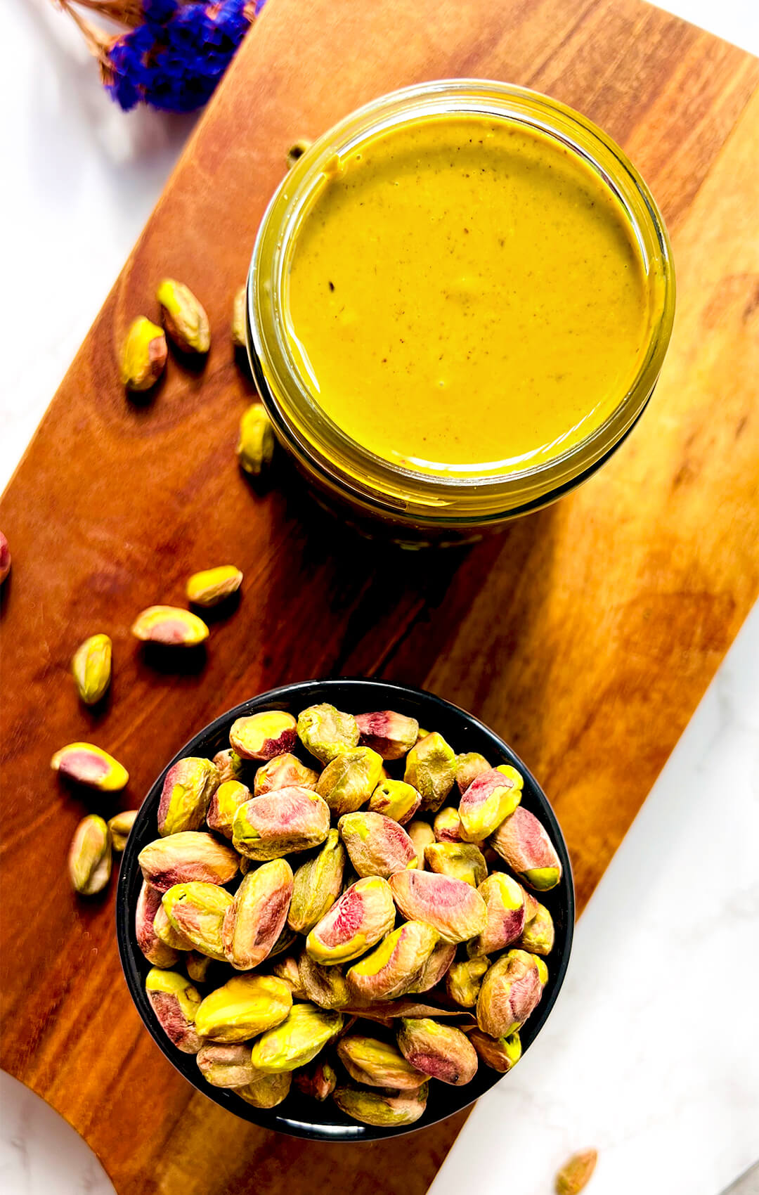 Top view of homemade pistachio butter in a jar beside a bowl of raw pistachios, showing the natural colour, creamy texture, and simple one ingredient homemade pistachio butter recipe.