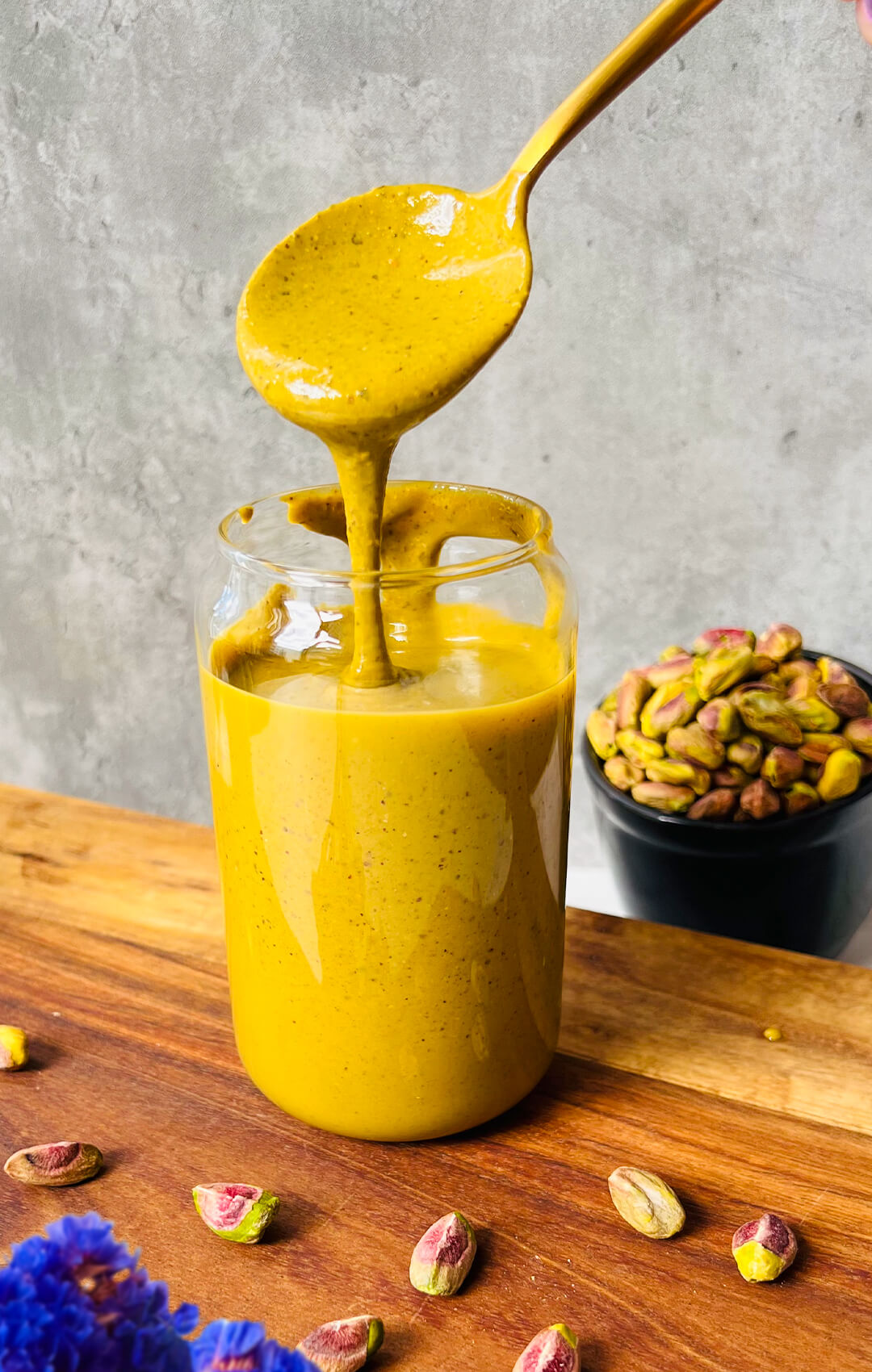 Glossy spoonful of homemade pistachio butter dripping back into a jar, showing the velvety smooth, drizzleable texture of this healthy one ingredient pistachio butter recipe.