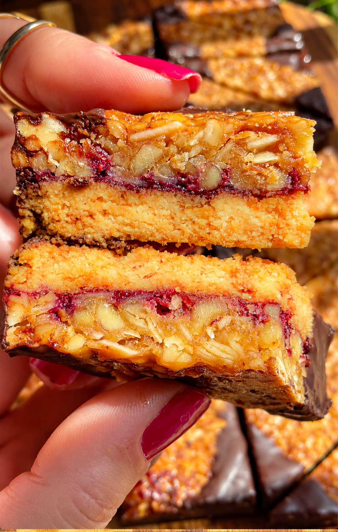 Close-up of two Almond Jam Crunch Cookie Corners showing soft almond shortbread, raspberry jam and a thick crunchy almond walnut layer.