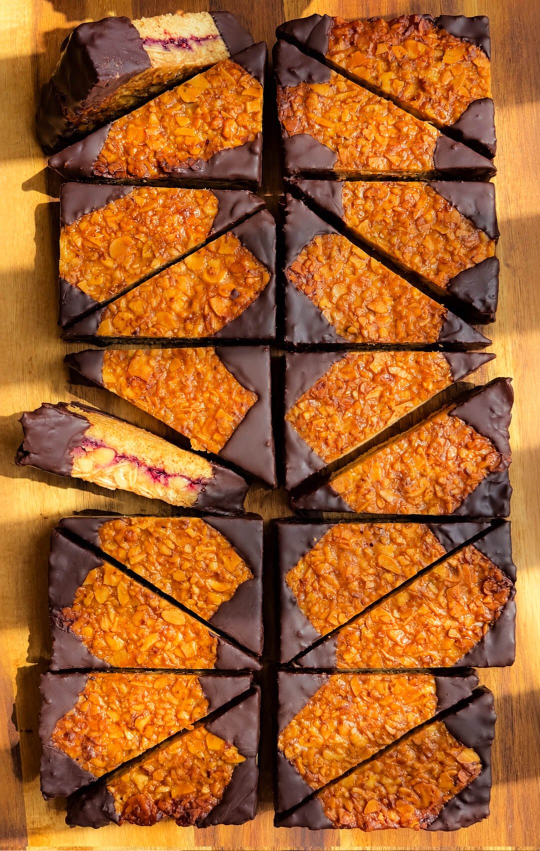 Gluten-free German Nussecken style cookie corners with raspberry jam, caramelized almond walnut topping and dark chocolate dipped edges.