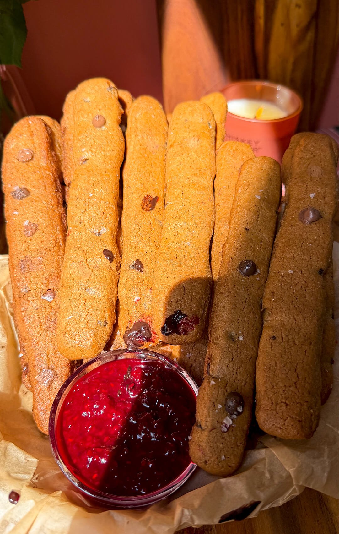 Golden gluten-free chocolate chip cookie fries made with almond flour arranged beside a bowl of glossy homemade raspberry jam.