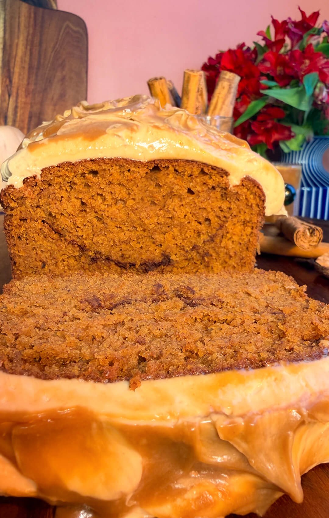 A thick slice of healthy pumpkin bread in front of the frosted loaf, showing its moist crumb, cinnamon sugar ribbon, and peanut butter cream cheese frosting with coconut caramel. An easy gluten-free, refined sugar-free recipe combining almond, oat, and lupin flours, coconut sugar, and brown monk fruit sweetener, with a sugar-free option.